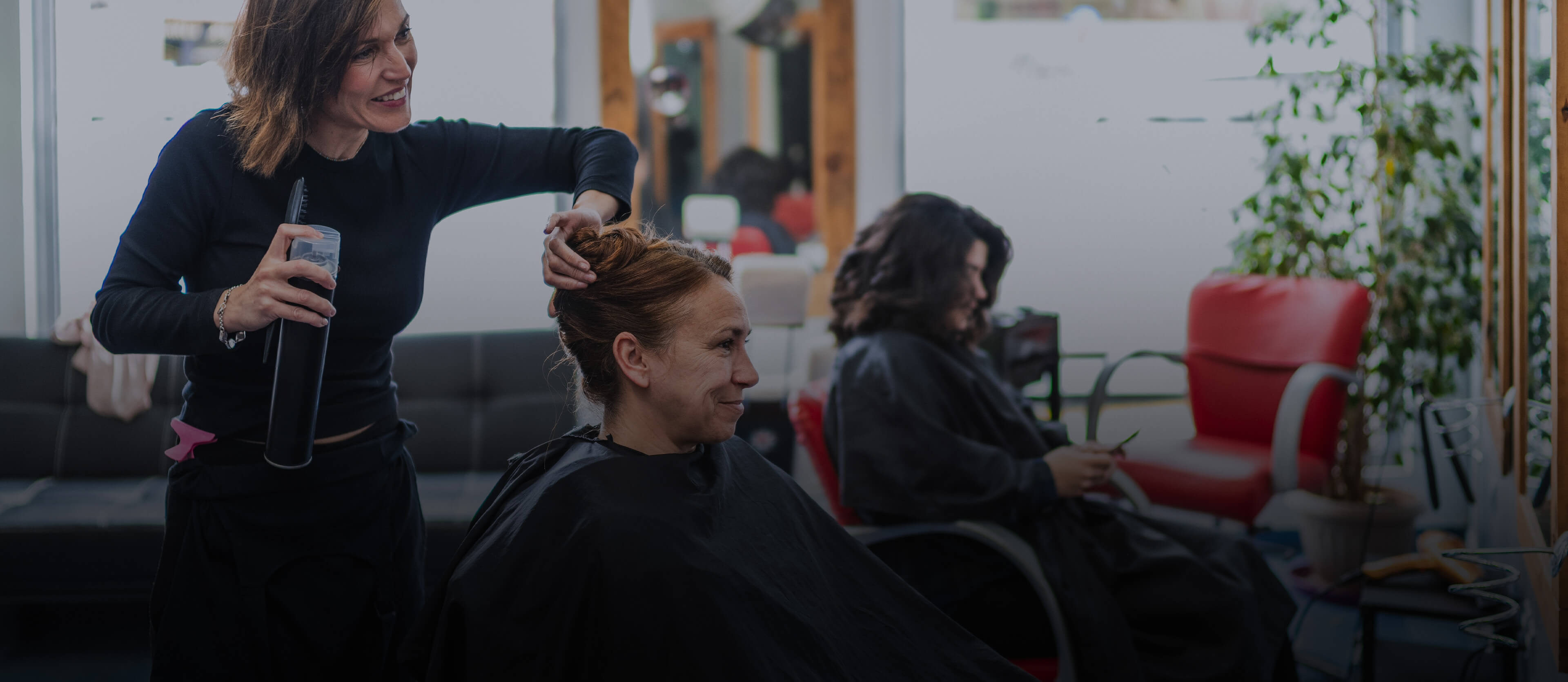 Woman getting her hair styled by another woman in a salon setting.